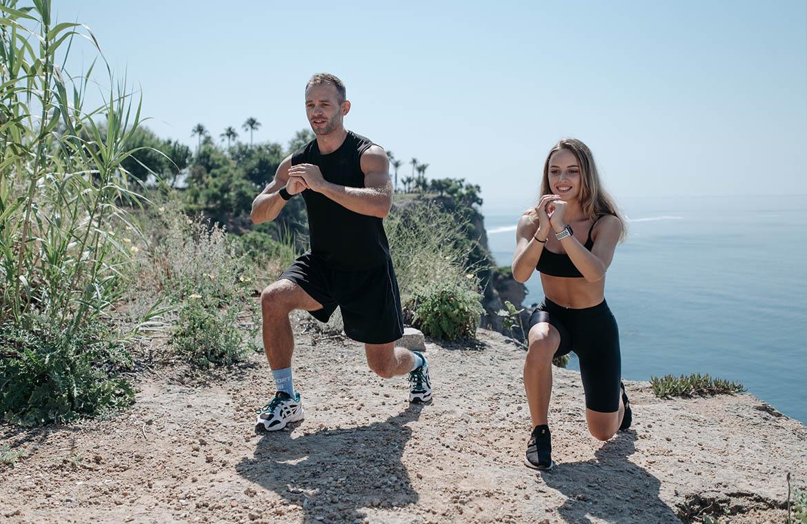 A man and a woman are exercising in sports attire on a cliff by the sea